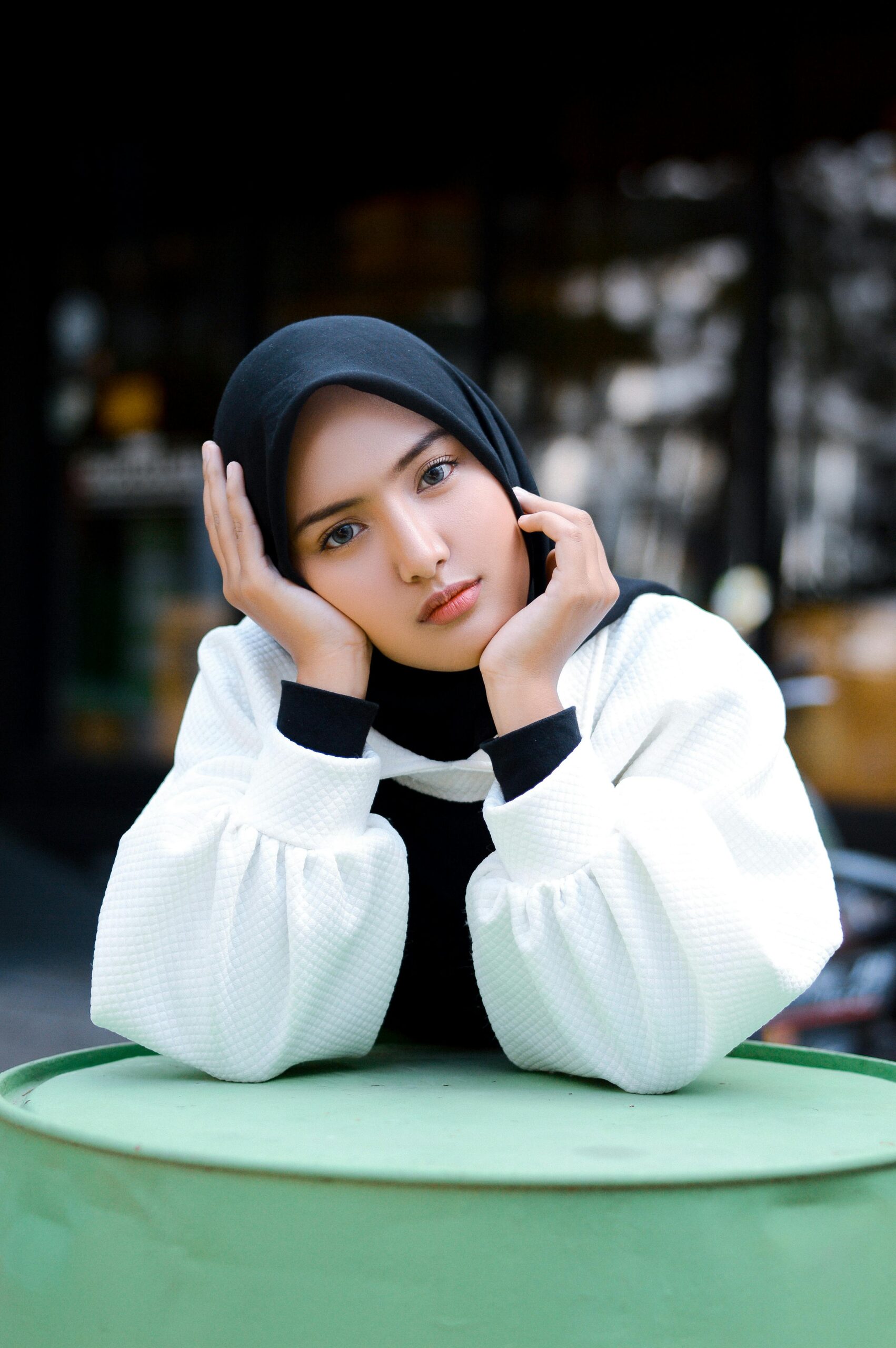A young woman wearing a hijab and white sleeves poses outdoors in Garut, Indonesia.